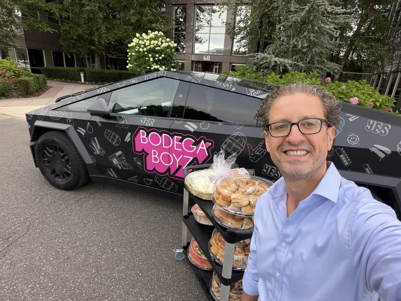 Jordan Isenstadt takes a selfie in front of a Bodega Boyz Cybertruck with bagel trays at the Long Island Bagel Bash